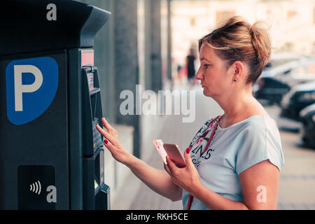 Acheter un billet pour femme à l'aide de stationnement par carte de débit ou téléphone mobile, debout à côté de la machine de stationnement Banque D'Images