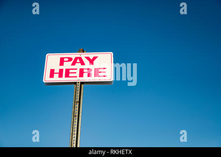 Payez ici pancarte en haut d'un mur extérieur avec des voitures en stationnement Banque D'Images