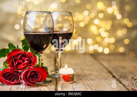 Concept de la Saint-Valentin. Deux verres de vin rouge, roses et bougie allumée sur une table rustique en bois en face d'un flou d'arrière-plan lumineux Banque D'Images