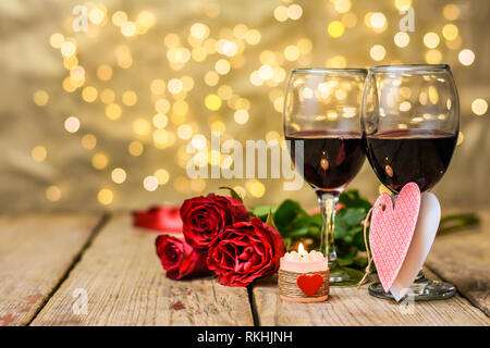 Valentine's Day still life. Deux verres de vin, les roses rouges, les messages et les bougies sur une table rustique en bois en face d'une zone lumineuse floue Banque D'Images