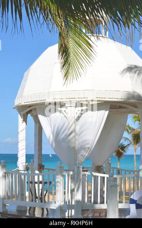 White wedding gazebo in a seaside tropical garden at a destination wedding reception with decorated chairs lined up for a civic ceremony. Banque D'Images