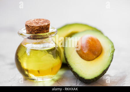 Bouteille d'huile d'avocat avec la moitié de l'avocat des fruits sur fond de béton, vert, aromatique, l'huile fraîche et saine Banque D'Images