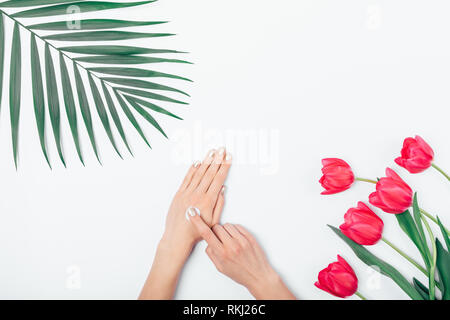 Mise à plat de l'arrangement woman's hands appliquer crème cosmétique à côté de la feuille de palmier et bouquet de tulipes roses sur le tableau blanc, vue du dessus. Banque D'Images