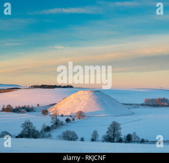 Silbury Hill dans la neige de l'hiver au lever du soleil. Avebury, dans le Wiltshire, Angleterre Banque D'Images