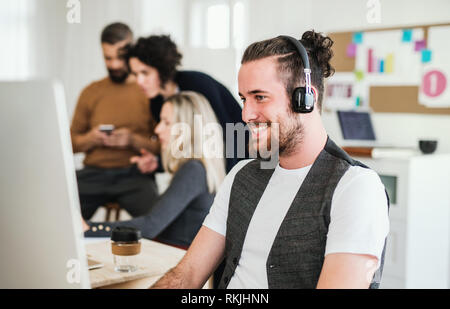 Jeune homme avec un casque et collègues dans un bureau moderne. Banque D'Images