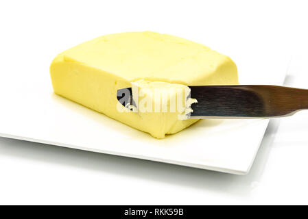 Morceau de beurre avec un couteau sur la plaque d'argent isolé sur un fond blanc en close-up Banque D'Images