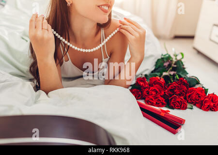 Jeune femme trouvés bouquet de roses avec des bijoux de perle en boite cadeau au lit. Happy girl essayer sur collier. Valentines Day surprise Banque D'Images