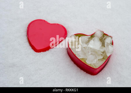 Gros plan d'une boîte rouge en forme de cœur, avec des cubes de glace à l'intérieur, fixé sur un fond de neige minimaliste. Banque D'Images