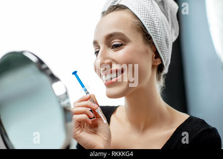 Portrait of a smiling woman blanchir les dents avec gel et les renforts en plastique, assis sur le canapé à la maison Banque D'Images