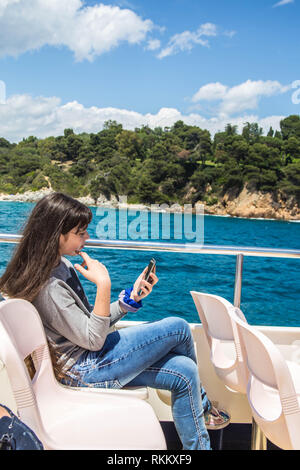 Une jeune fille aux cheveux longs se penche sur le téléphone tout en étant assis sur un bateau de plaisance. Banque D'Images