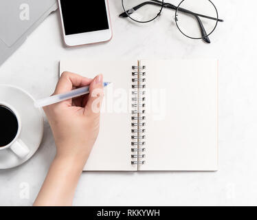 Une femme est isolé sur la rédaction de notes de travail bureau stylisé en bureau avec ordinateur portable, smartphone, verres et café, maquette, vue de dessus, flatlay, copie Banque D'Images