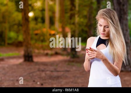 Belle blonde jeune femme dans le parc au coucher du soleil de l'envoi de message sur téléphone mobile - Image Banque D'Images