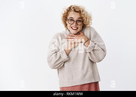 Fille heureuse et reconnaissante de doux sourire tendre la main cadeaux sur la poitrine en reconnaissant et heureux de poser avec une surprise sincère sourire Banque D'Images