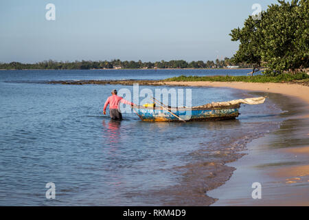 Pêcheur cubain se retire son vieux bleu bateau à voiles ferlées le matin de la plage de sable dans l'espoir d'attraper quelques poissons. Cuba Banque D'Images