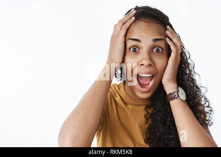 Close-up shot de Ravi étonné professionnels africains-américains femme avec les cheveux bouclés tomber jaw hurler de l'enthousiasme et la joie tenant les mains sur la tête Banque D'Images