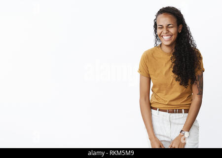 Studio shot of african american female charismatique sans souci avec cool tattoo fermer les yeux comme rire et sourire avoir in awesome Banque D'Images