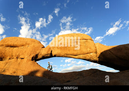 La mère et le fils de marcher sous l'arche de roche naturelle, près de la montagne de granit Spitzkoppe, Namibie, Afrique Banque D'Images