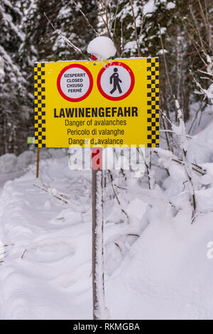 Panneau d'avertissement jaune-noir et les panneaux en allemand, anglais, italien et français : fermé, Danger d'avalanche. Une forêt couverte de neige, dans les montagnes de la route. Banque D'Images