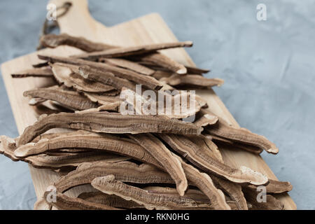 Tranches de champignons lingzhi séché, également appelé le reishi (Ganoderma lucidum), ou sur une planche en bois, fond gris. La médecine traditionnelle chinoise produit. Banque D'Images