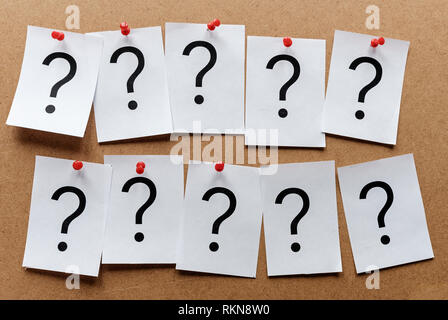 Deux rangées de points d'interrogation imprimé sur les cartes blanches épinglées sur un tableau d'affichage en bois avec des punaises Banque D'Images