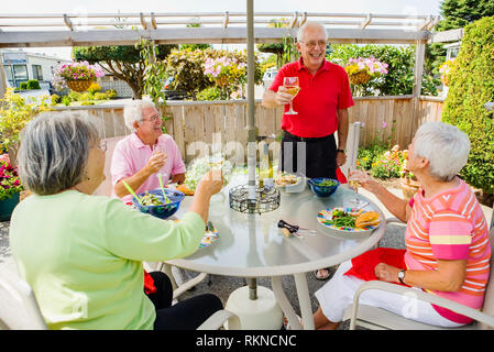 Deux couples matures appréciant un repas à l'extérieur sur leur terrasse avec un verre de vin. Banque D'Images