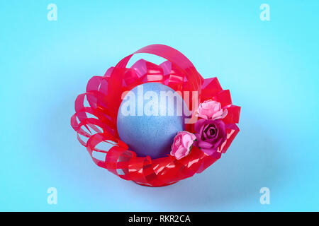 Oeuf de Pâques Diy panier fait de plastique rouge décoré de fleurs artificielles fond bleu. Idée cadeau décoration, Printemps, Pâques. Étape par étape. Haut de page vi Banque D'Images
