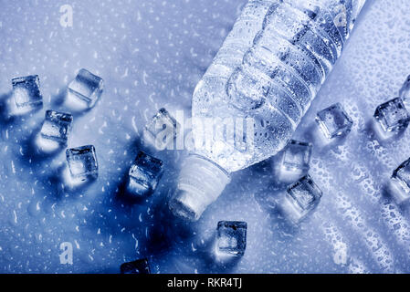 Boire de l'eau minérale fraîche en bouteille en plastique avec des cubes de glace et gouttes glacé. Concept de vie sains à partir de ci-dessus. Banque D'Images