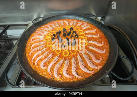 Une paella aux fruits de mer la cuisine dans une casserole noire sur le sommet d'une cuisinière à gaz dans une cuisine de restaurant à Valence, en Espagne. Banque D'Images