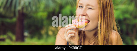 Portrait of a young woman eating a donut contre un arrière-plan de l'usine Banner, format long Banque D'Images