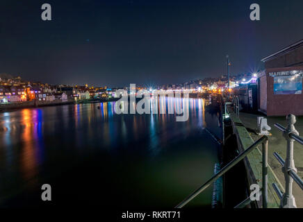 Une scène de la ville et le port de Whitby allumé jusqu'à la nuit. Les chambres lumineuses, lumières colorées se reflètent dans l'eau et un ciel sombre est ci-dessus. Banque D'Images