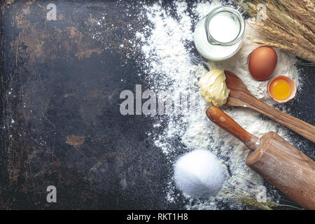 Cuire la pâte de recettes ingrédients oeufs, farine, lait, beurre, sucre et de rouleau à pâtisserie sur fond sombre. Avec l'arrière-plan de l'espace texte libre Banque D'Images