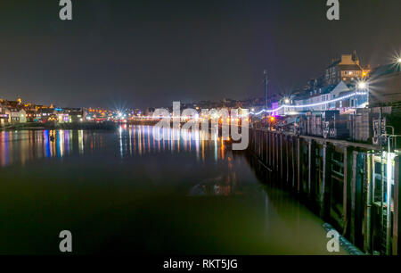 Une scène de la ville et le port de Whitby allumé jusqu'à la nuit. Les chambres lumineuses, lumières colorées se reflètent dans l'eau et un ciel sombre est ci-dessus. Banque D'Images