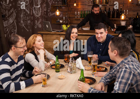 Groupe de jeunes amis assis autour de la table en bar togethe. L'humeur joyeuse. Banque D'Images