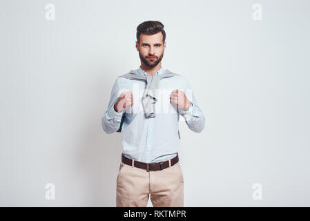 Superman. Confiant et bel homme avec les poings fermés près de la poitrine tout en se tenant à l'arrière-plan gris. Close-up Banque D'Images