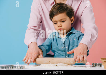 Cute little boy rouler la pâte avec mère sur fond bicolore Banque D'Images