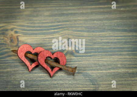 Deux coeurs en bois reliés ensemble avec de petits clous rouillés. Découper des cœurs en bois peints en rouge, vue en gros plan sur fond de bois avec cop Banque D'Images