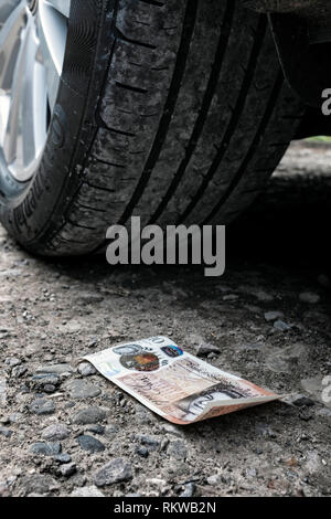 10 livres sterling sur le sol à côté d'une voiture en stationnement. Banque D'Images