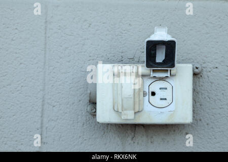 Vieille prise électrique nord-américaine rustique sur un mur extérieur en brique gris Banque D'Images