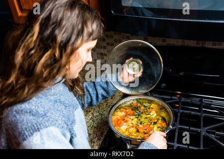 Gros gros pot de soupe aux légumes maison et femme en remuant sur comptoir en granit haut de cuisine en conteneur en acier inoxydable sur la cuisine cuisinière à gaz Banque D'Images