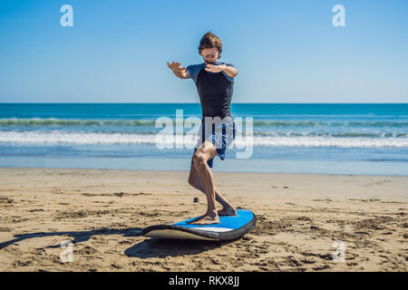 Jeune homme surfer formation avant de passer à queue sur une plage de sable. Apprendre à surfer. Locations de concept. Vacances d'été. Le tourisme, le sport Banque D'Images