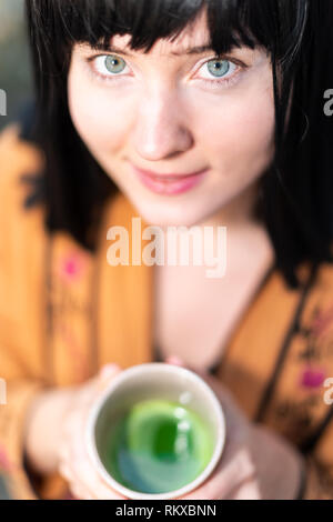 Femme Jeune fille aux cheveux noirs happy smiling holding thé vert matcha cup face closeup extérieur, caucasien yeux Banque D'Images