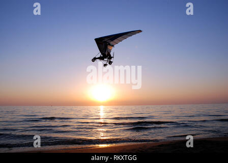 Ultralight trike vole de décisions et évolutions passe bas sur la plage au coucher de soleil à la fin de l'été Banque D'Images