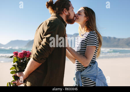 Man holding Flowers derrière et d'embrasser sa petite amie sur la plage. Couple amoureux, baiser sur la plage. Banque D'Images
