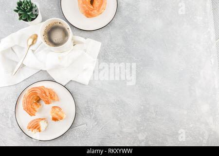 Le petit-déjeuner avec anneaux - chou à la crème, pâte à choux et tasse de café noir sur fond clair Banque D'Images