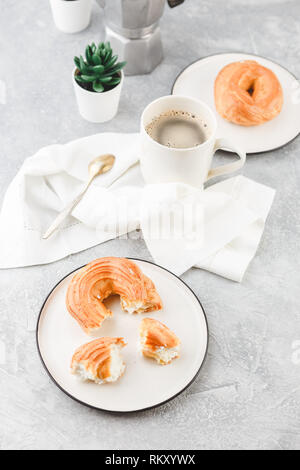 Le petit-déjeuner avec anneaux - chou à la crème, pâte à choux et tasse de café noir sur fond clair Banque D'Images