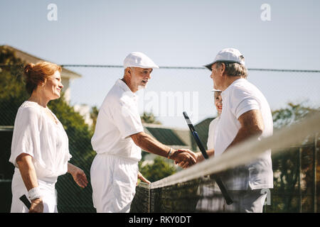 Senior men shaking hands standing on tennis après le match. Chaque message d'aînés d'autres après une partie de tennis en double mixte, debout près de la n Banque D'Images
