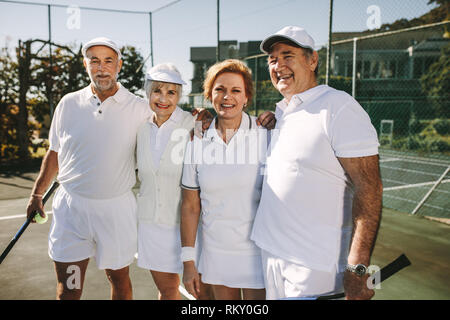 Les personnes âgées se tenant ensemble se tenant sur un court de tennis. Les aînés debout sur un court de tennis à jouer un match de double mixte. Banque D'Images