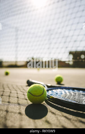 Tir au niveau du sol d'une raquette de tennis avec des balles sur un court de tennis. raquette de tennis et balles placées à côté d'un filet sur un court de tennis par une journée ensoleillée. Banque D'Images