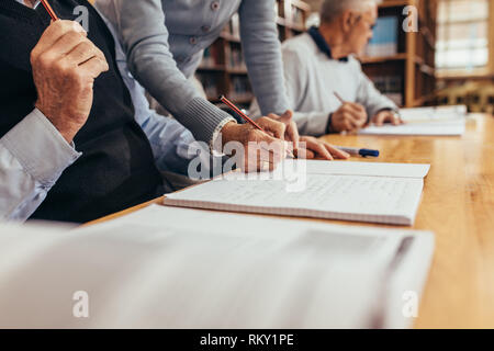 Cropped shot d'un maître de l'écriture dans le carnet d'un homme dans la salle de classe. Des personnalités de l'université d'apprentissage assis dans une classe avec un Banque D'Images