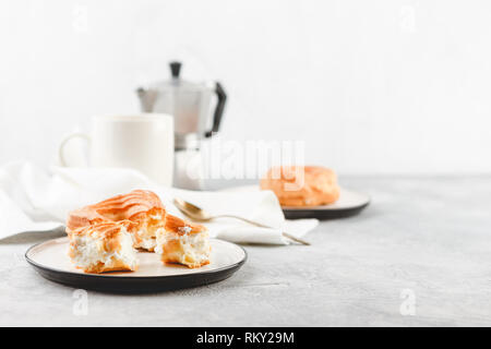 Le petit-déjeuner avec anneaux - chou à la crème, pâte à choux et tasse de café noir sur fond clair Banque D'Images